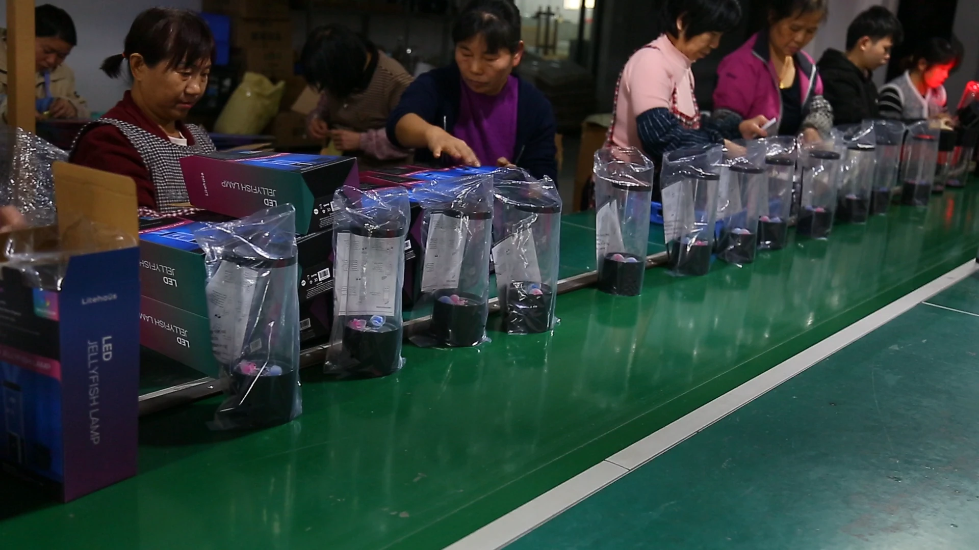 明雄员工在包装线上整理套有保护袋的灯具,旁边摆放着彩盒