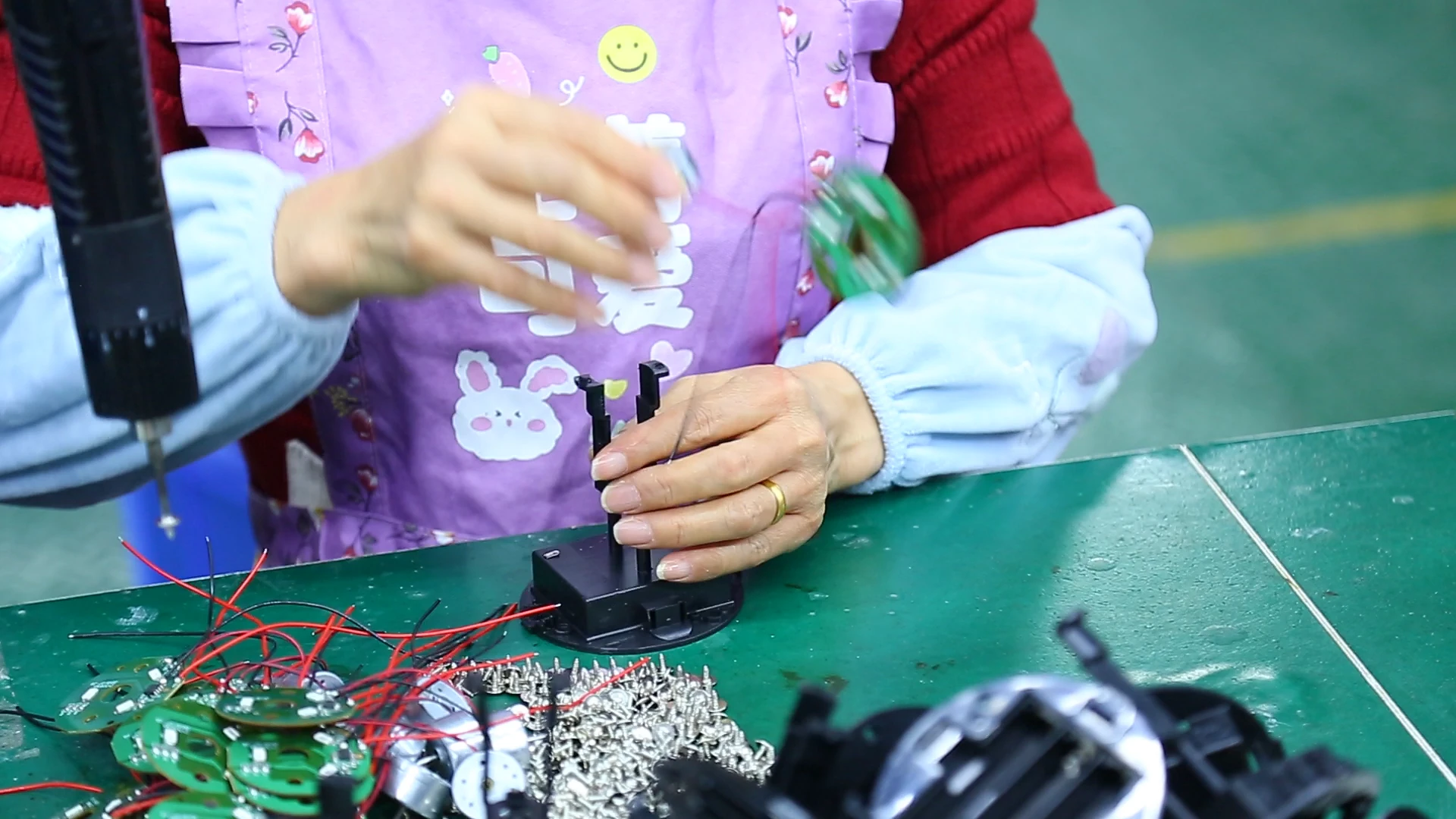 员工在绿色工作台上用工具装配灯具部件,台面摆放着电路板